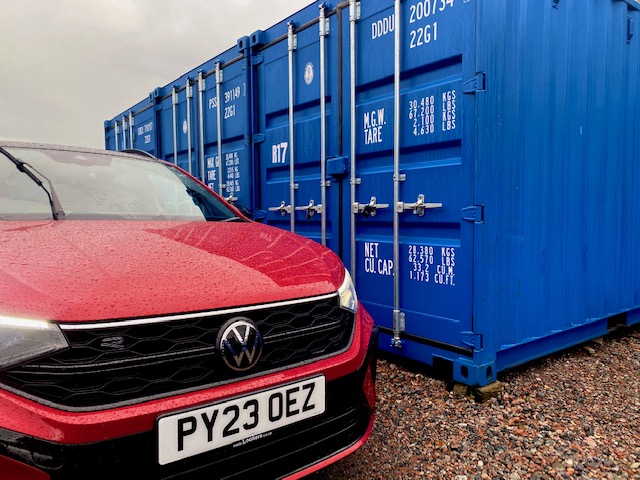 a car parked next to a row of shipping containers