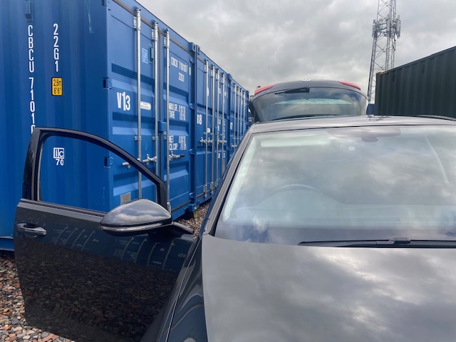 a car with door and boot open parked next to self storage units
