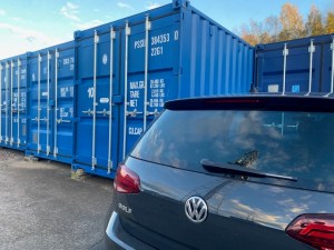 a car parked next to four shipping containers