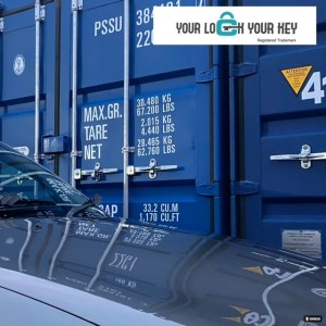 two shipping containers with the front of a car in the foreground