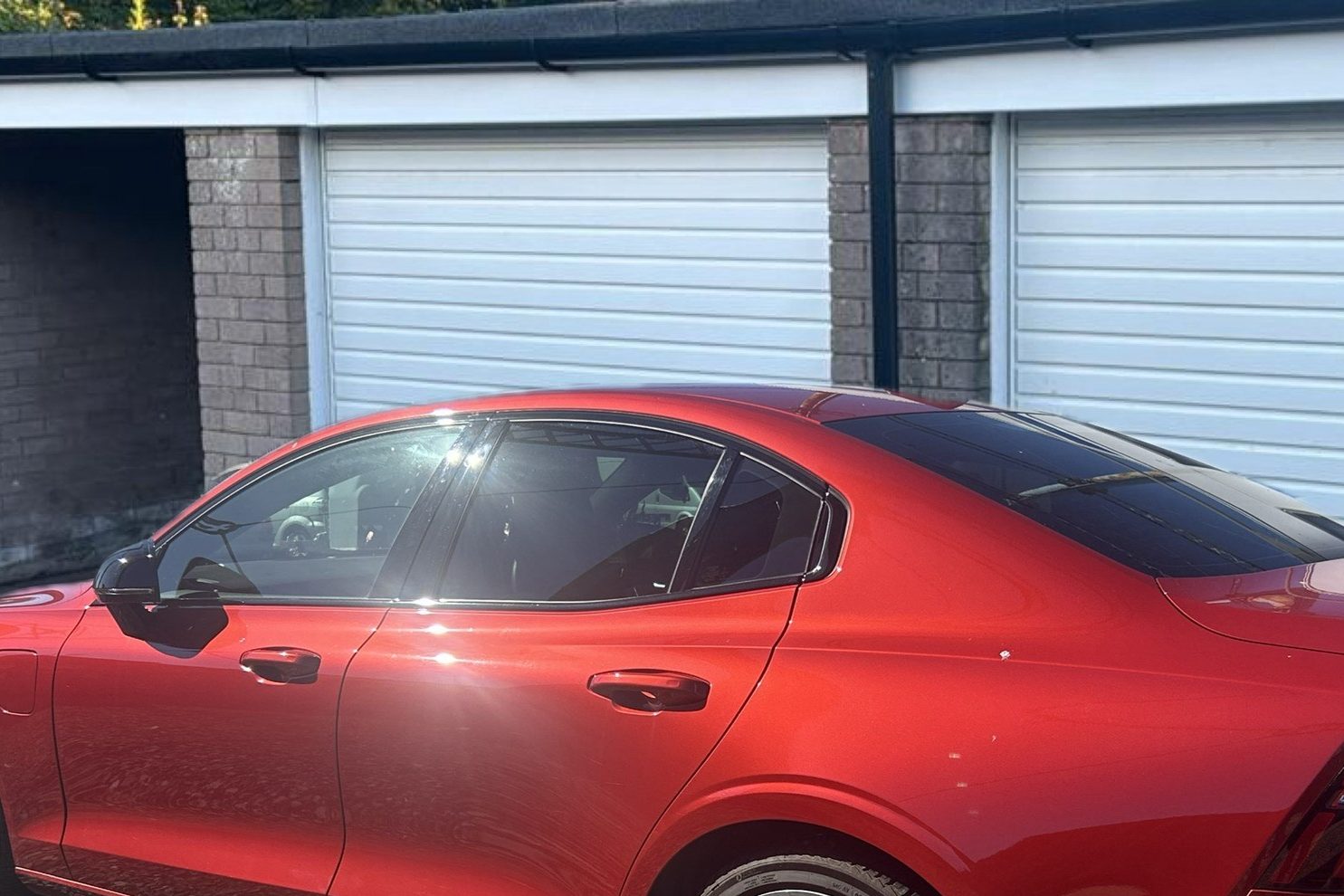 A red car parked in front of garage doors.