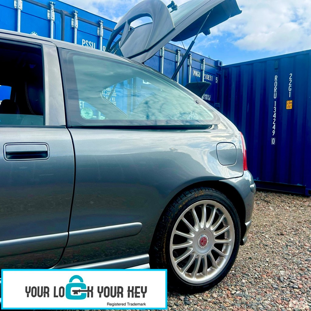 a car with its boot lid open parked next toa shipping container