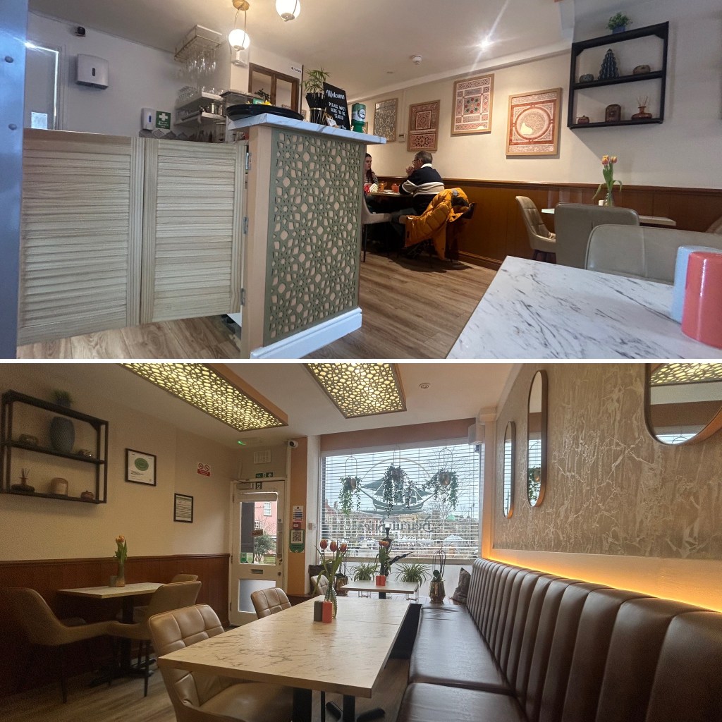 Interior view of a cozy restaurant featuring a wooden counter with decorative paneling and seating arrangements. The space includes framed art, potted plants, and a warm ambiance.