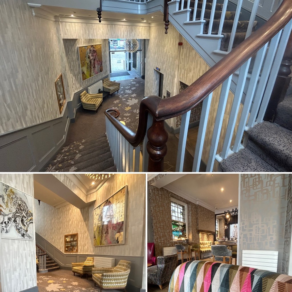 View of a stylish hotel lobby featuring a staircase, decorative wall art, and seating areas.